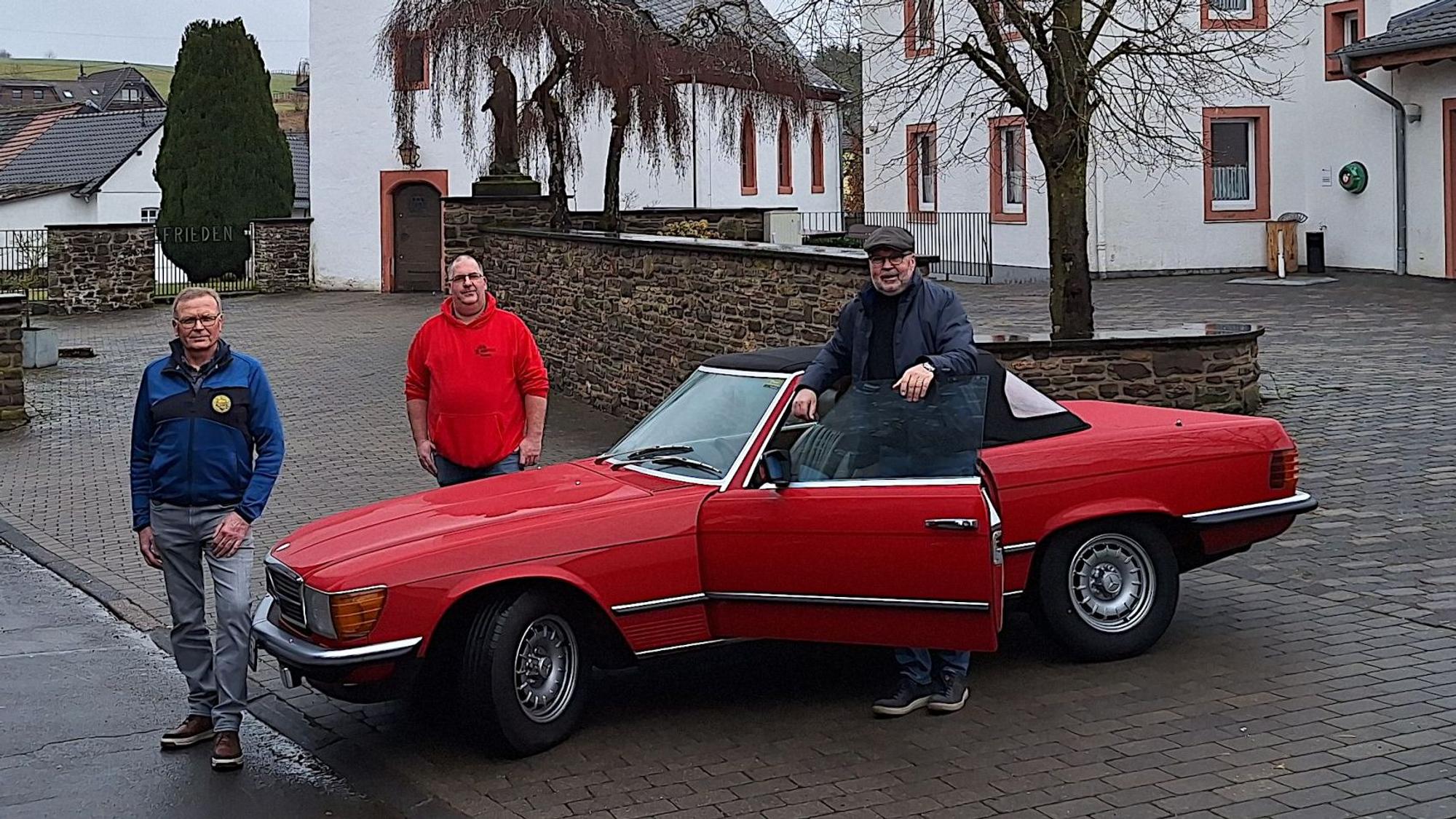 Drei Männer stehen an einem roten Mercedes Oldtimer-Cabrio.