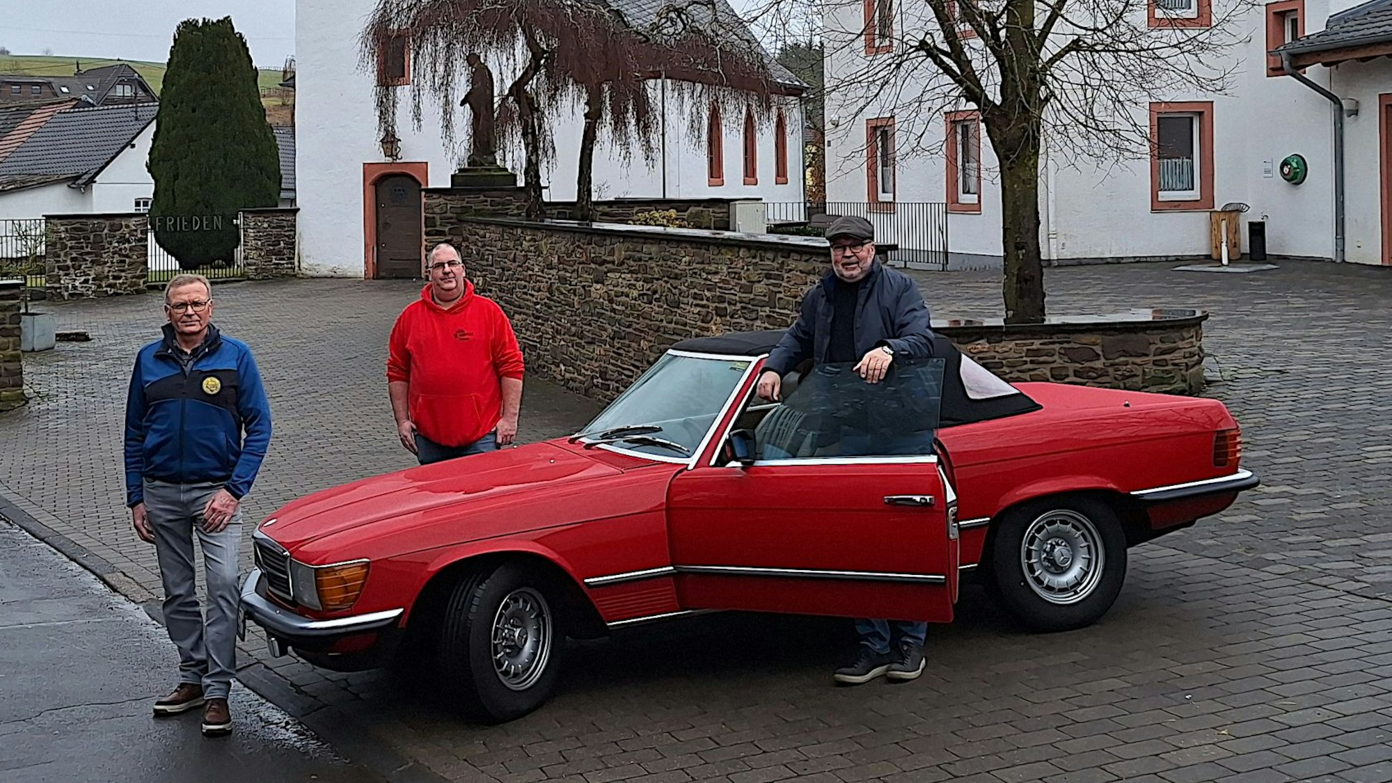 Drei Männer stehen an einem roten Mercedes Oldtimer-Cabrio.