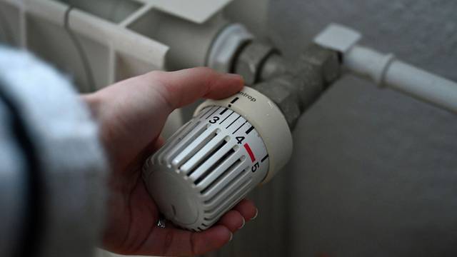 ILLUSTRATION - 24.02.2026, Berlin: Eine Frau dreht an einem Thermostatregler einer Heizung in einer Wohnung.