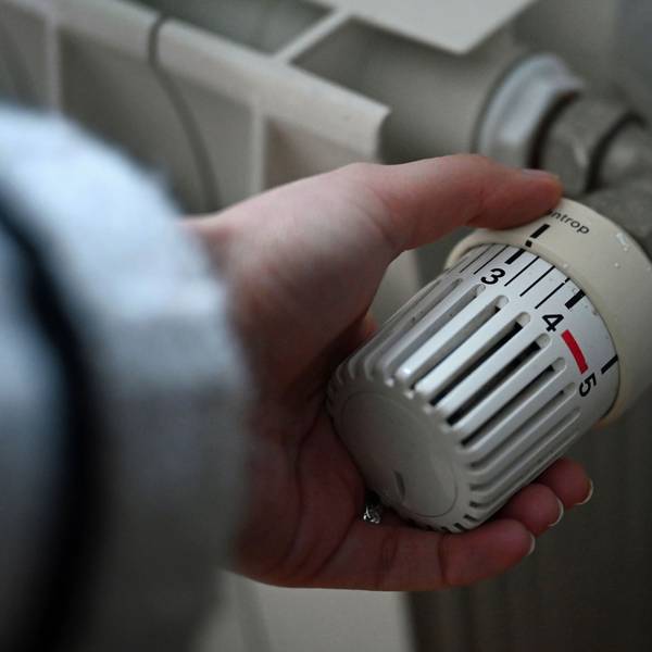ILLUSTRATION - 24.02.2026, Berlin: Eine Frau dreht an einem Thermostatregler einer Heizung in einer Wohnung.