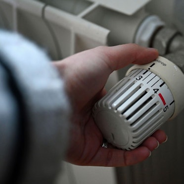 ILLUSTRATION - 24.02.2026, Berlin: Eine Frau dreht an einem Thermostatregler einer Heizung in einer Wohnung.