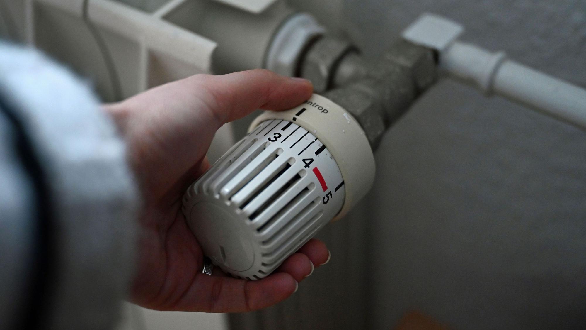 ILLUSTRATION - 24.02.2026, Berlin: Eine Frau dreht an einem Thermostatregler einer Heizung in einer Wohnung.