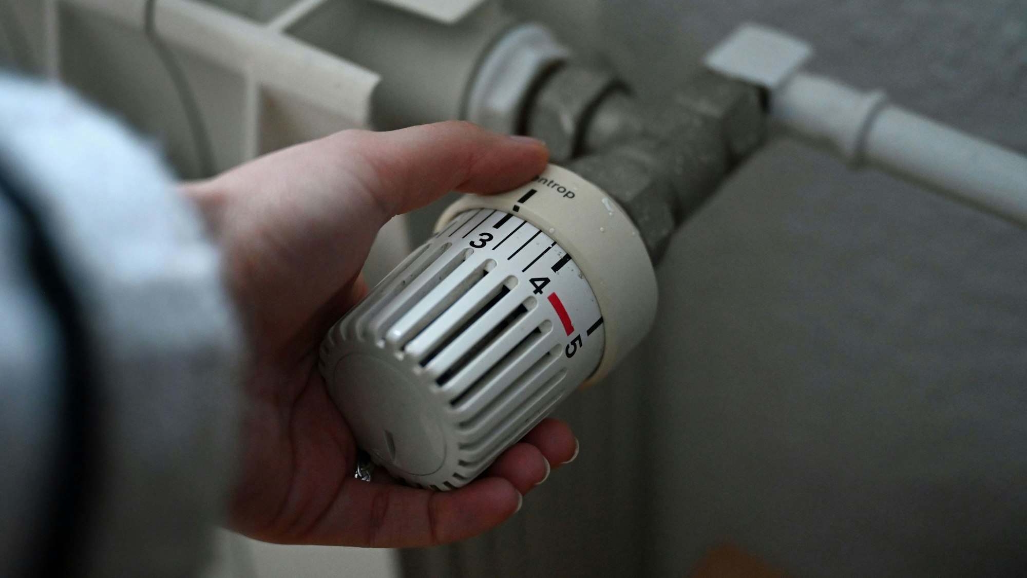 ILLUSTRATION - 24.02.2026, Berlin: Eine Frau dreht an einem Thermostatregler einer Heizung in einer Wohnung.