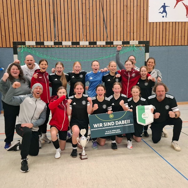Spielerinnen und Betreuer jubeln. Sie hocken beziehungsweise stehen in zwei Reihen vor einem Tor.