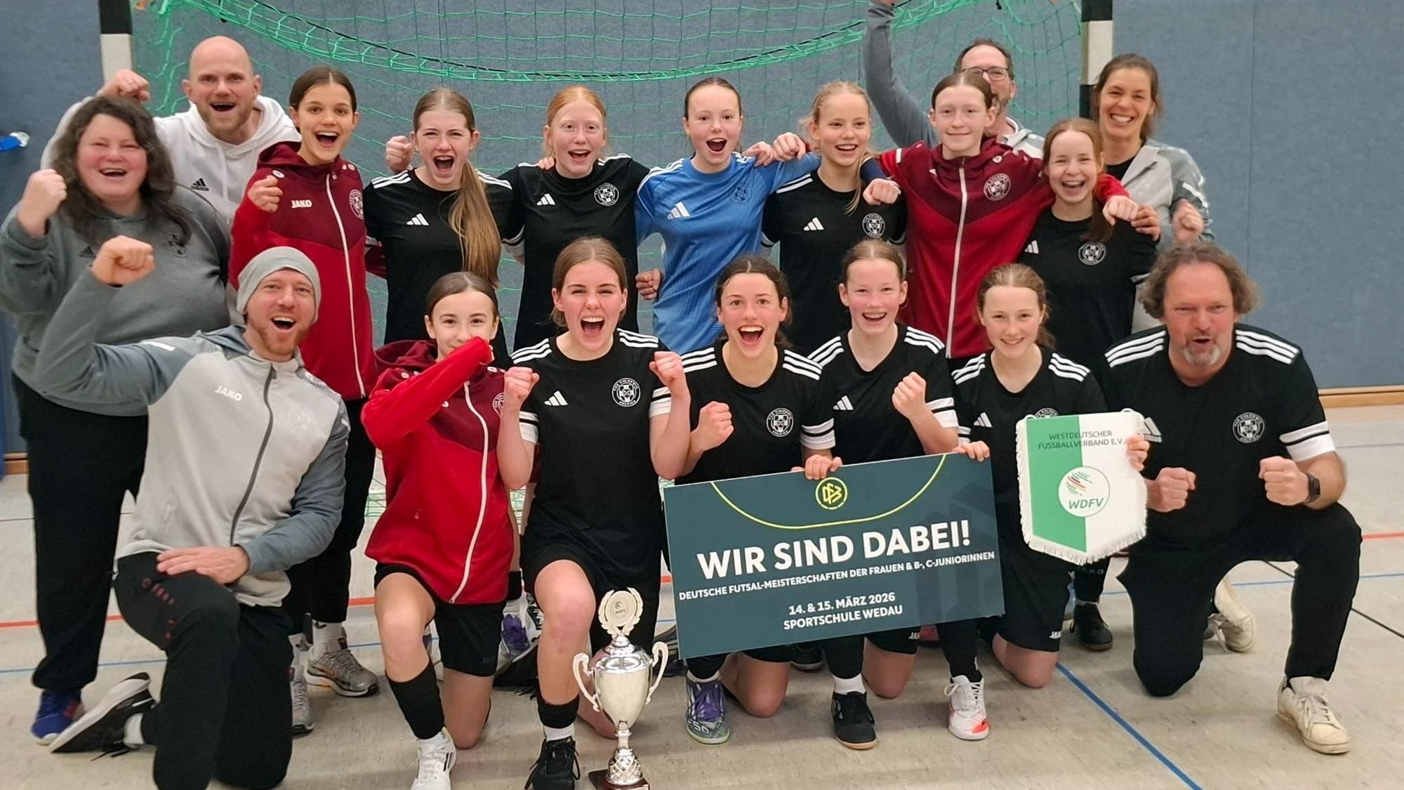 Spielerinnen und Betreuer jubeln. Sie hocken beziehungsweise stehen in zwei Reihen vor einem Tor.