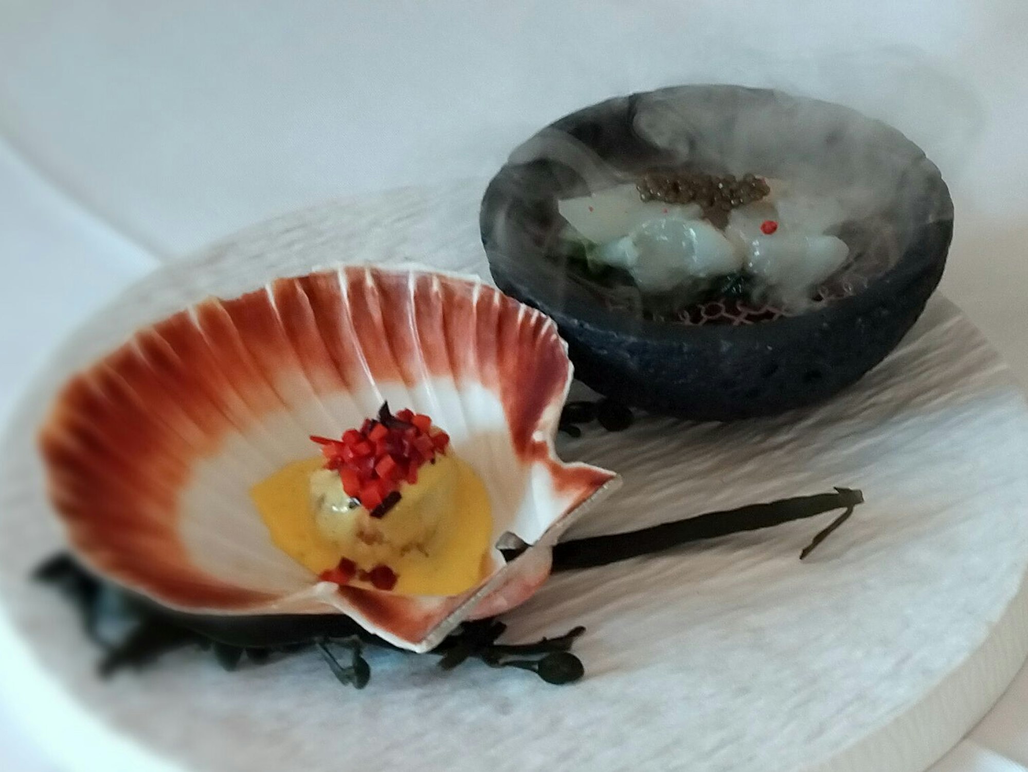 Perle des Meeres: Die gebratene Jakobsmuschel vorn hat ein Häubchen von Möhren-Blaubeer-Tatar. Die über Hickory-Holz geräucherte Jakobsmuschel liegt auf Pak Choi und unter Stör-Kaviar.