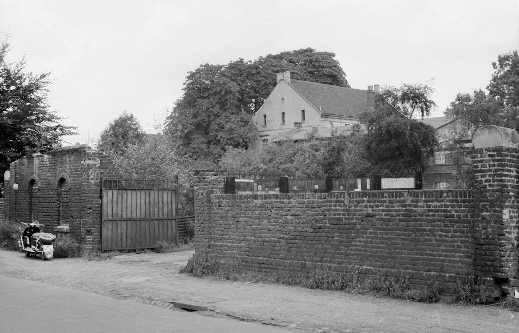 Hinter einer Mauer liegt ein Gutshof mit mehreren Gebäuden.