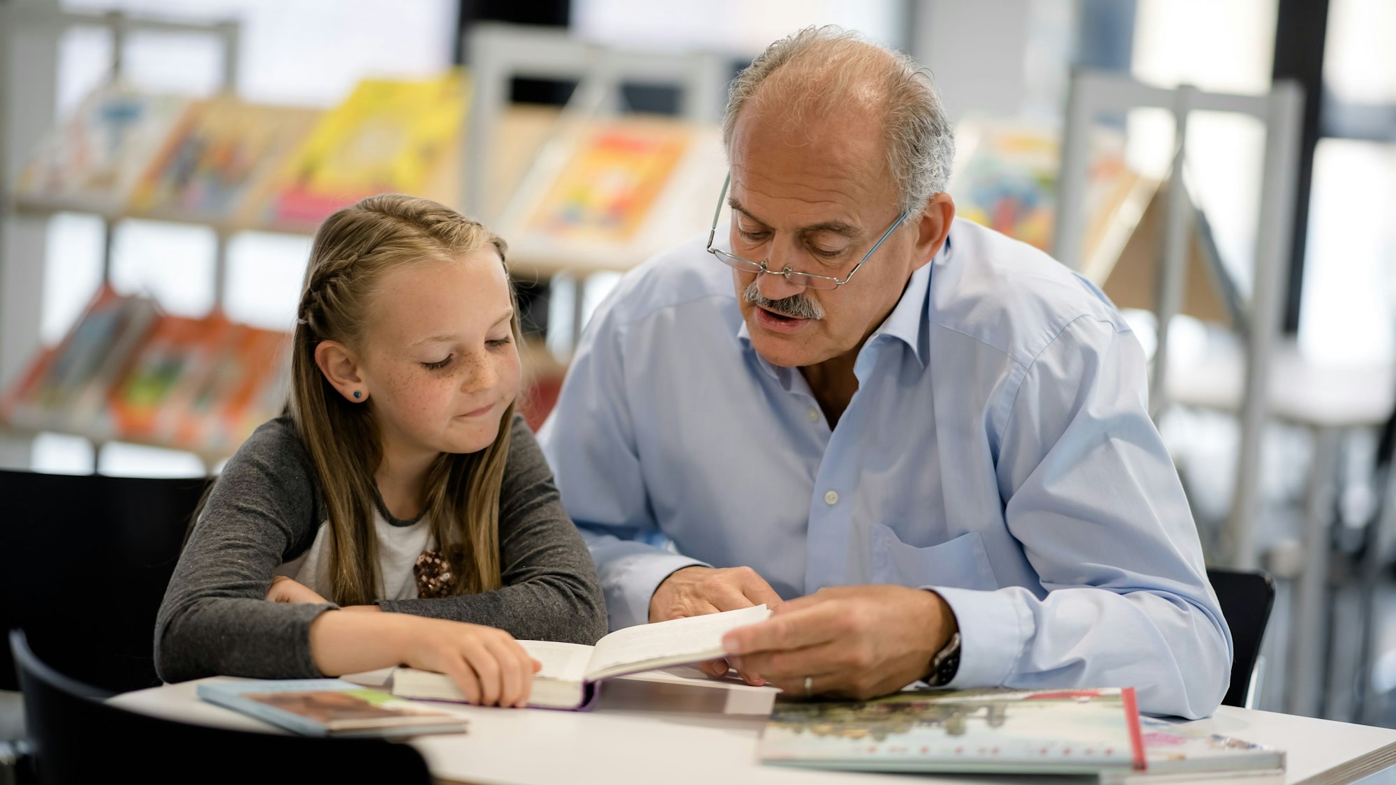 Ein älterer Herr liest einem Kind vor.