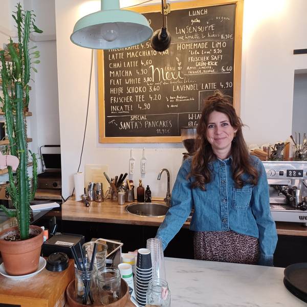 Eine Frau mit langen dunklen Haaren steht hinter der Theke eines Cafés.