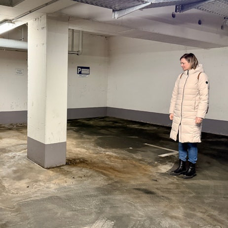 Eine Frau aus der Eigentümergemeinschaft steht im Parkhaus und blickt auf den Boden.