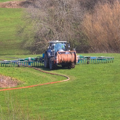 Foto eines Traktors, der mit speziellen Schläuchen Gülle auf einer Wiese verteilt