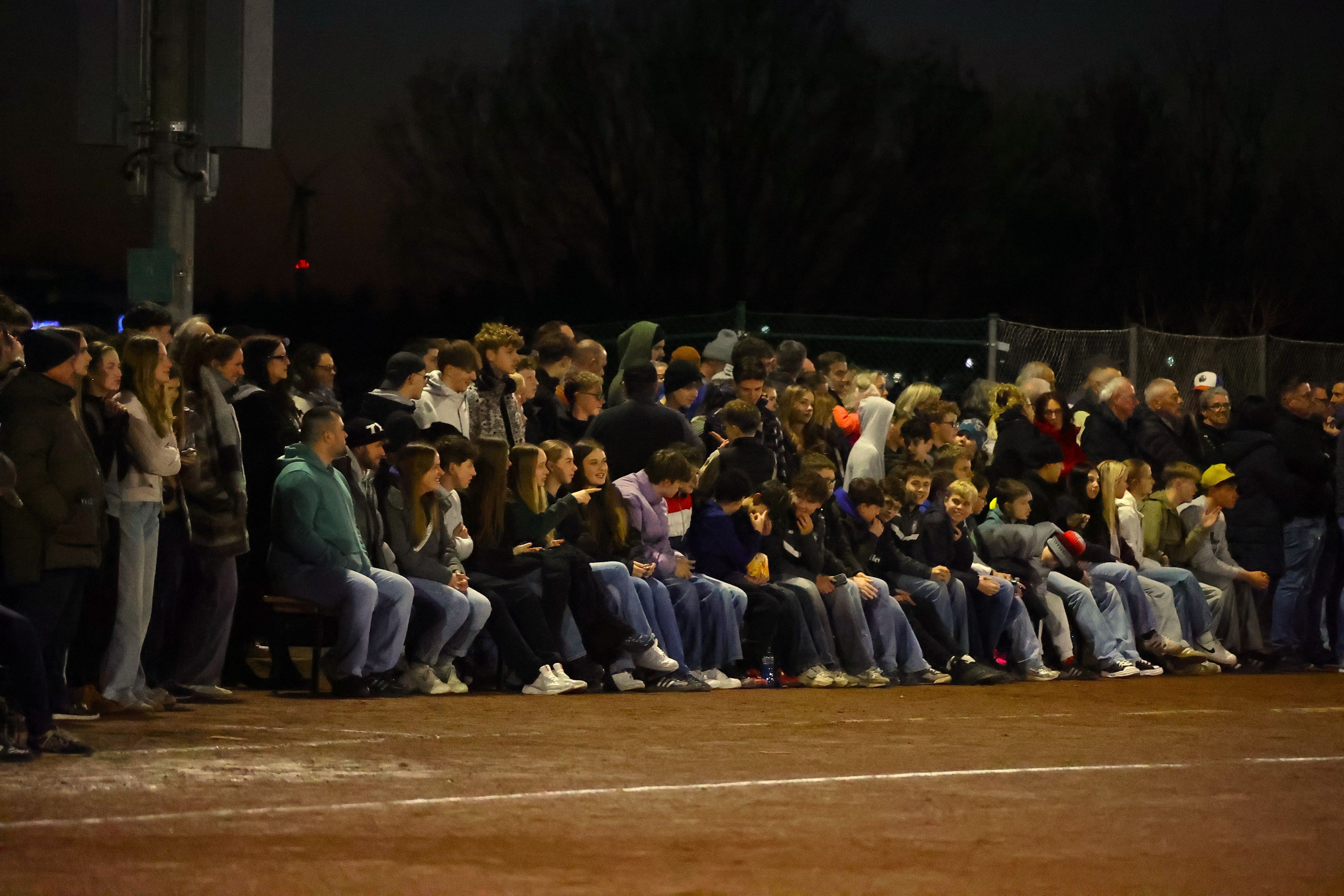 Zahlreiche Zuschauer sitzen und stehen am Spielfeldrand.