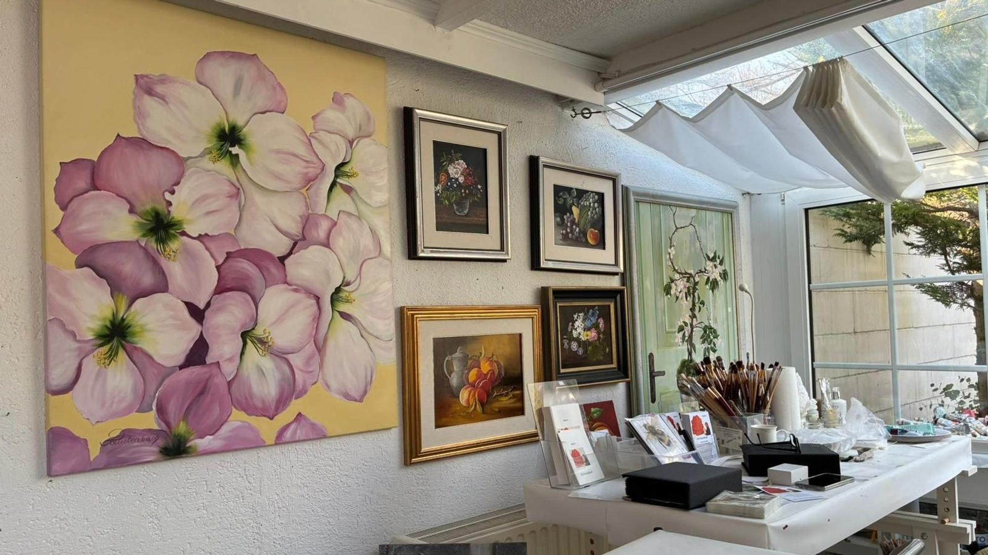 Im Atelier hängen viele Bilder von Blumen, auf einem Tisch stehen Pinsel und Farben.