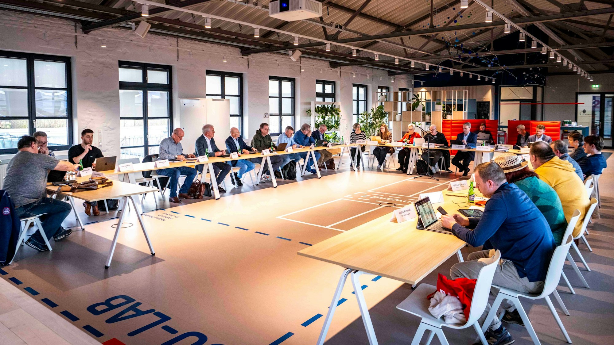 Das Bild zeigt einen Moment der Ausschusssitzung in der Ideenfabrik. Zahlreiche Politikerinnen und Politiker sitzen an Tischen.