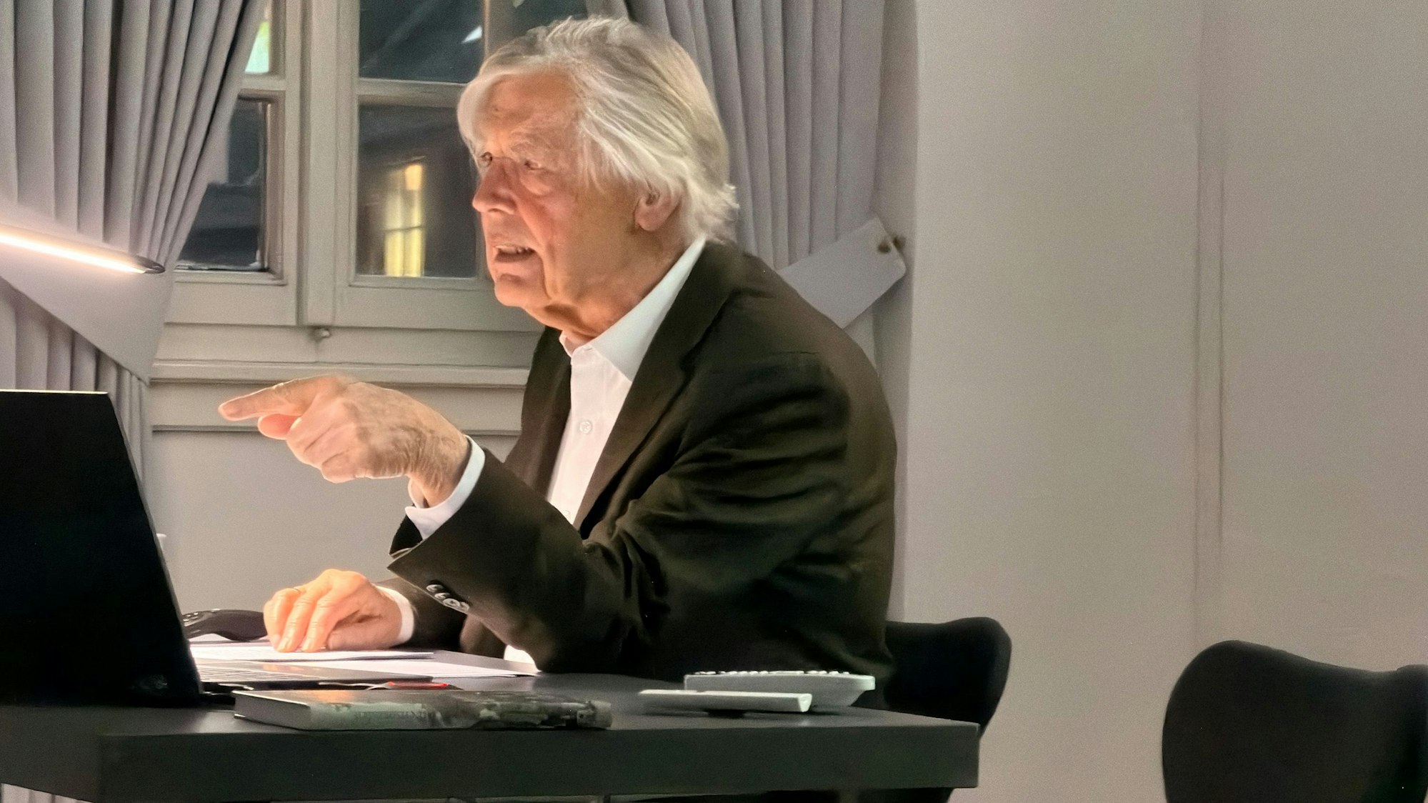 Ein weißhaariger Mann sitzt während eines Vortrags an einem Tisch.