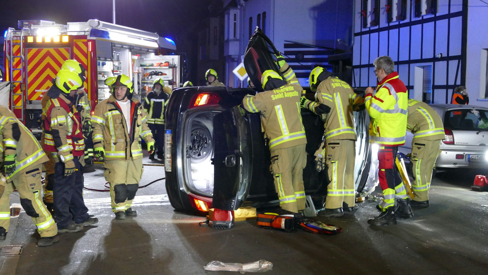 Feuerwehrleute in Sankt Augustin stehen an einem Fahrzeug, das auf der Seite liegt.
