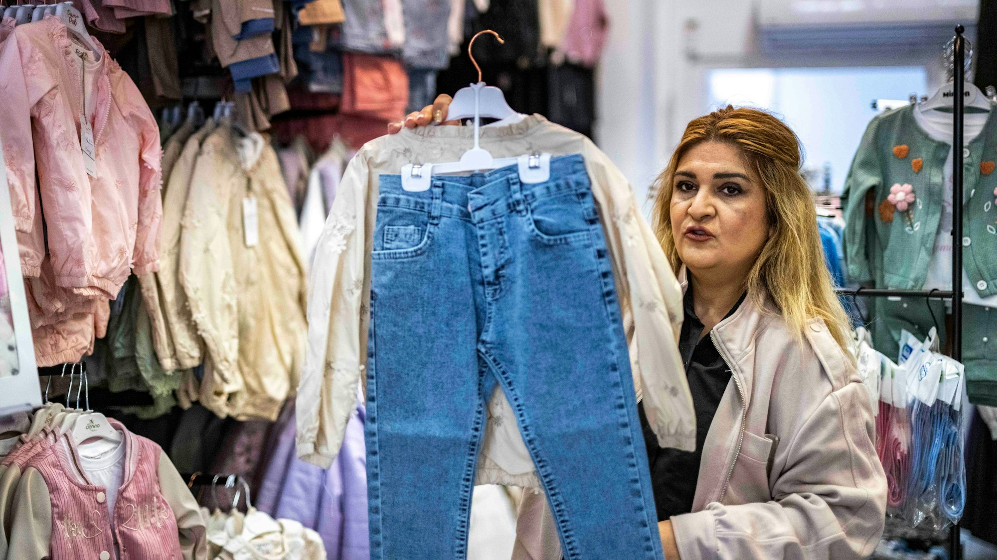 Das Bild zeigt Savda Käsken, die ein Outfit für Kinder in die Kamera hält.