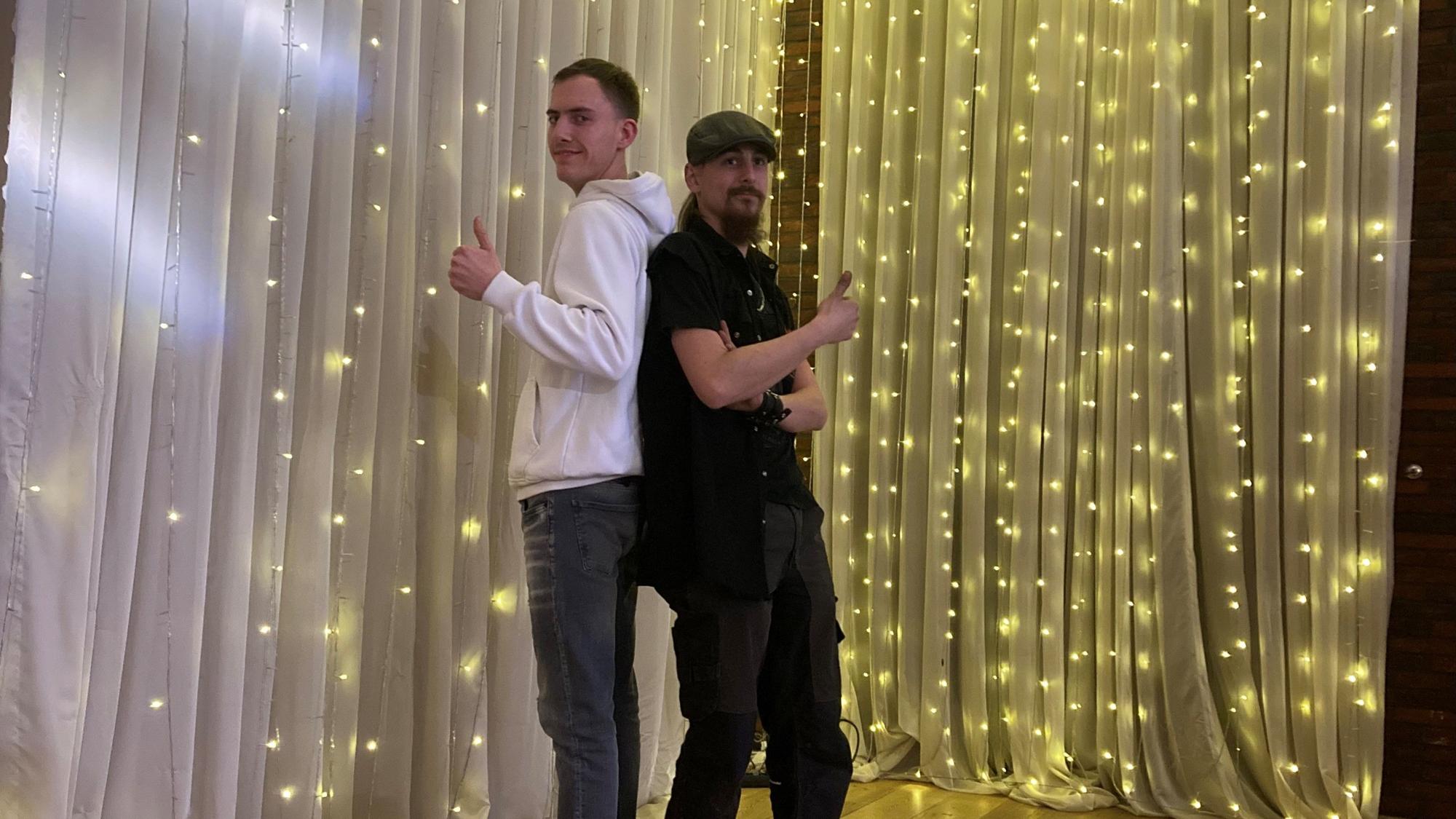 Das Foto zeigt zwei junge Männer vor einer Lichterkette.