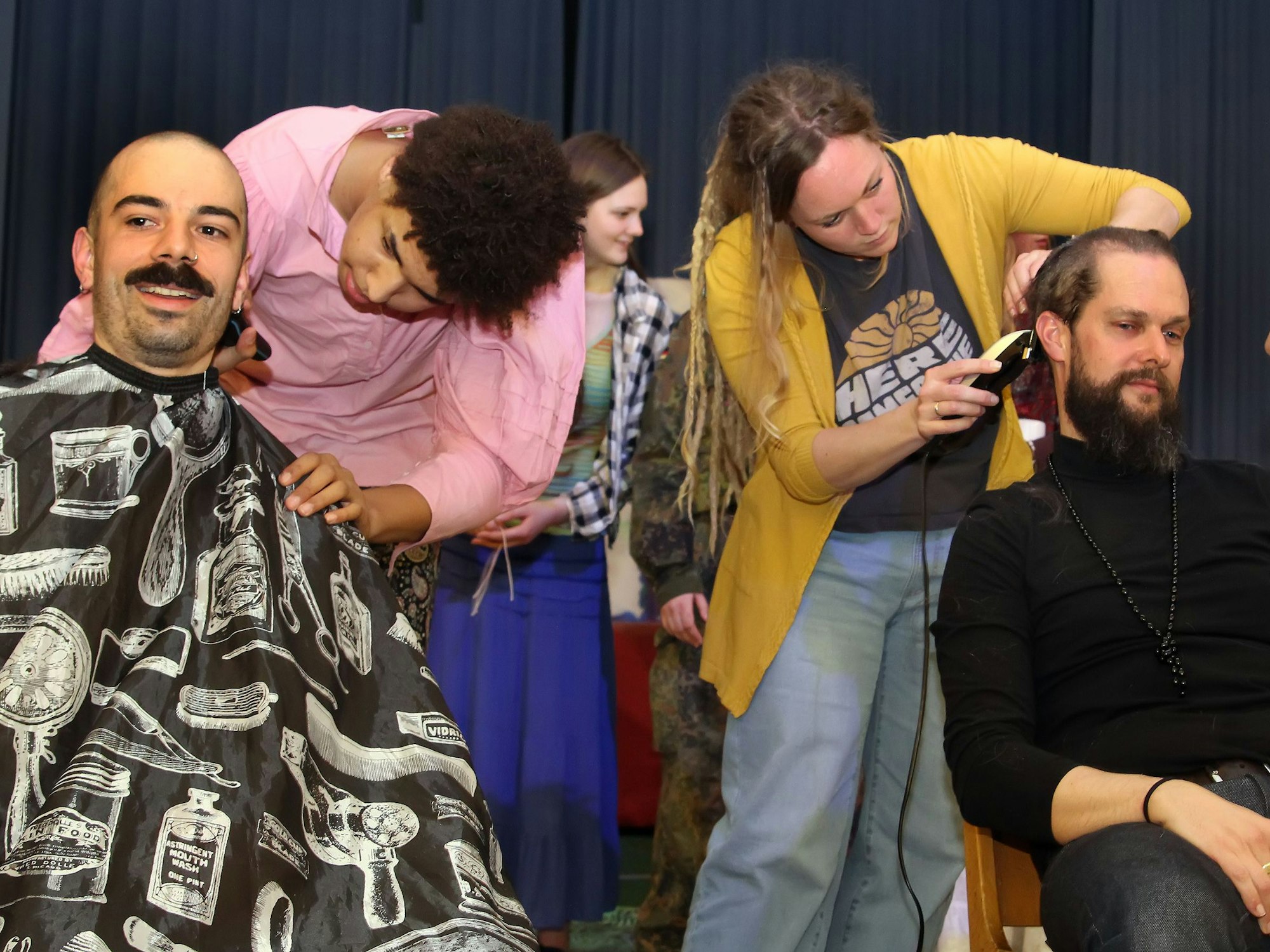 Das Bild zeigt zwei Lehrer der Waldorfschule, die von Schülerinnen die Haare abrasiert bekommen.