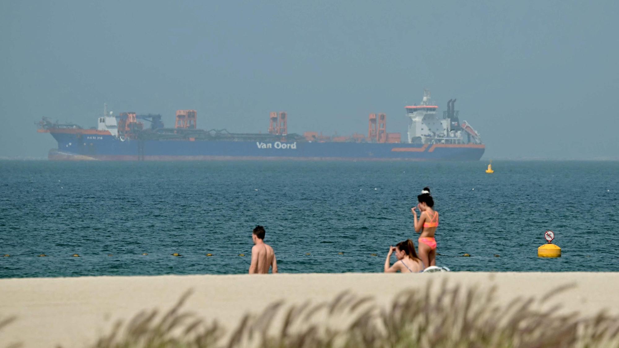 Menschen entspannen sich am Strand, während vor der Küste Dubais am 2. März Frachtschiffe vor Anker liegen. Der Krieg mit dem Iran hat Auswirkungen auf den Tourismus.
