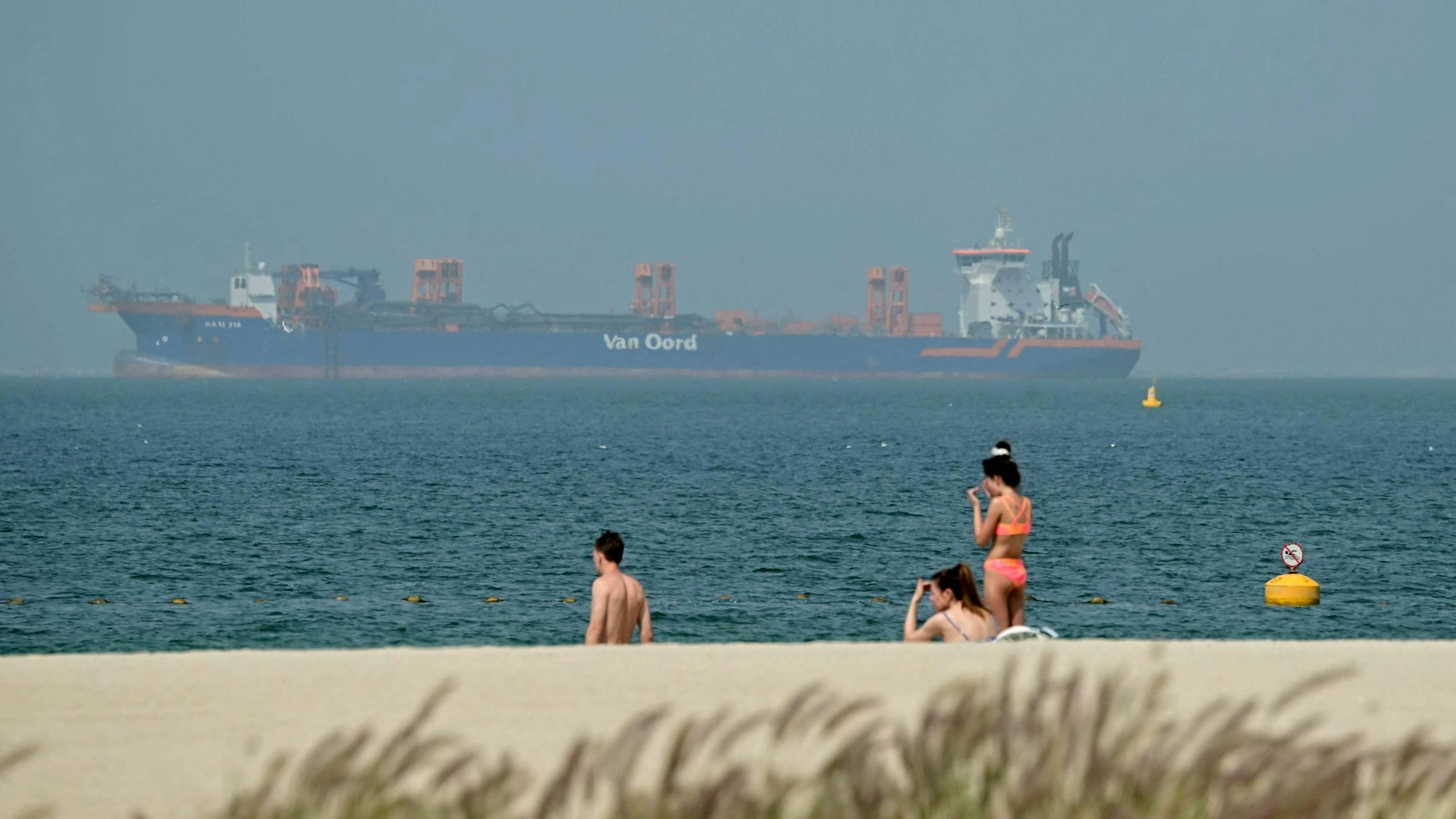Menschen entspannen sich am Strand, während vor der Küste Dubais am 2. März Frachtschiffe vor Anker liegen. Der Krieg mit dem Iran hat Auswirkungen auf den Tourismus.