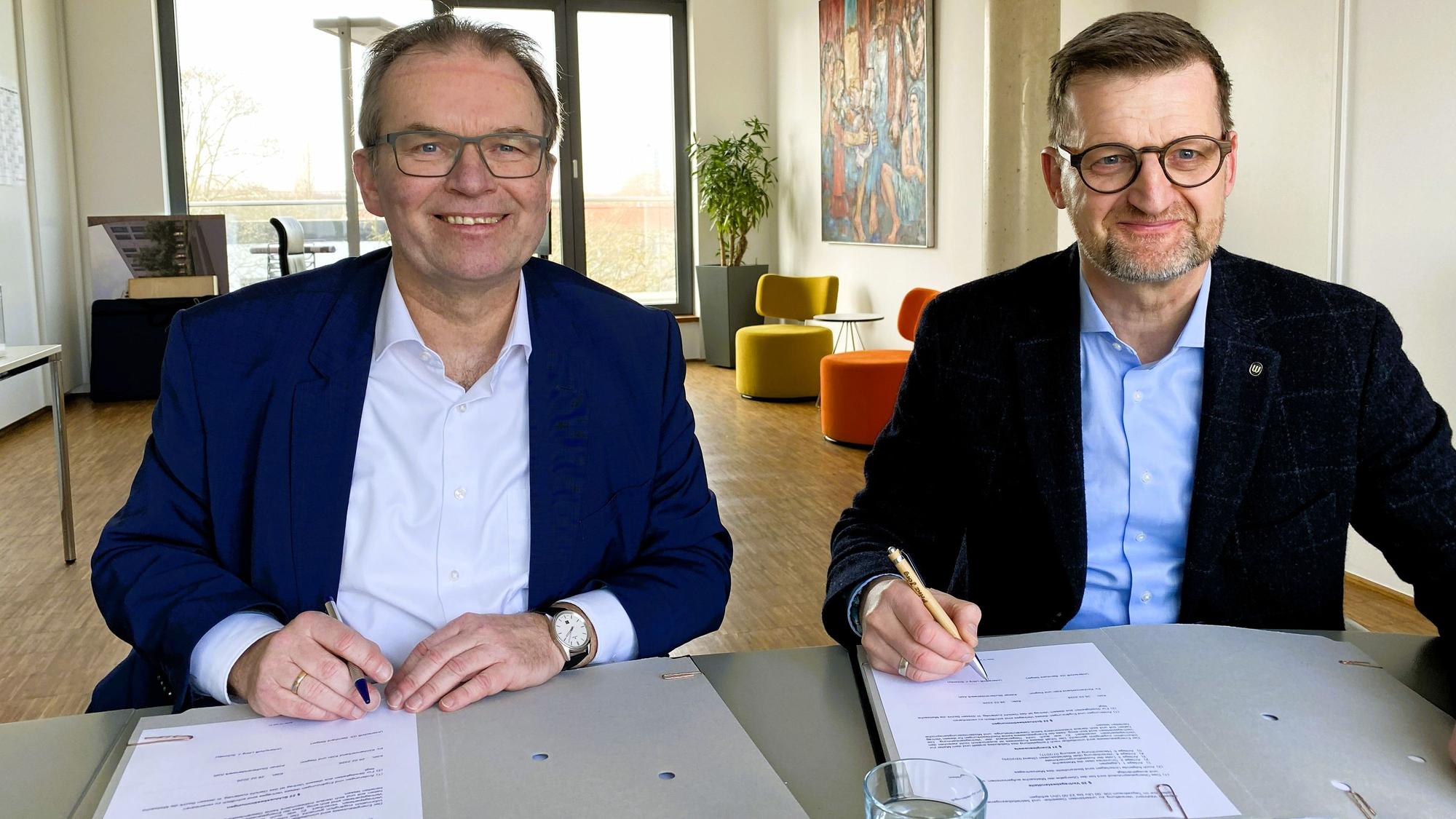 Zwei Männer sitzen an einem Tisch und unterzeichnen Schriftstücke