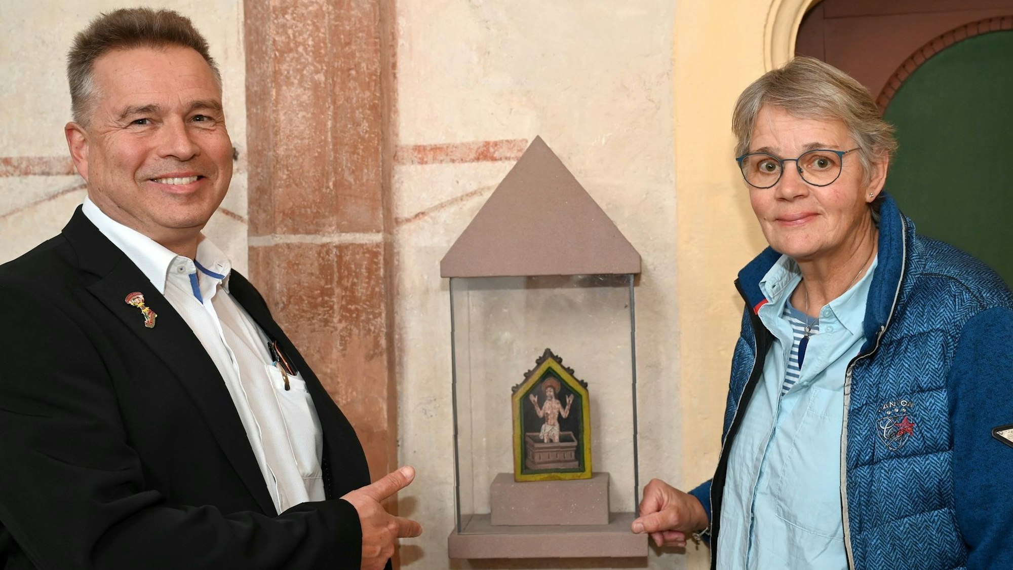 Claudia Müller und Peter Schweikert-Wehner stehen in einer Kirche am Hosteler Pax-Täfelchen.