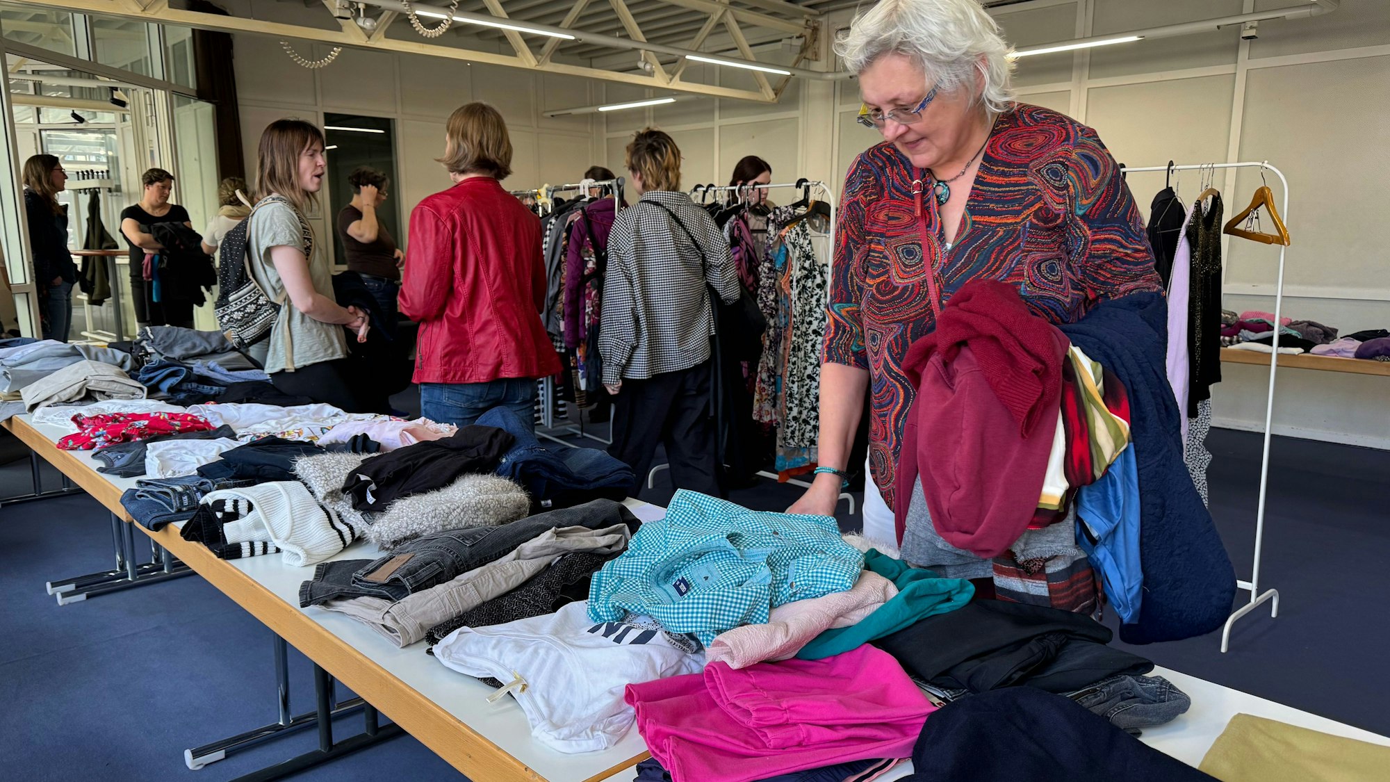 Eine Frau schaut sich Kleidung an, die auf einen Tisch liegt.