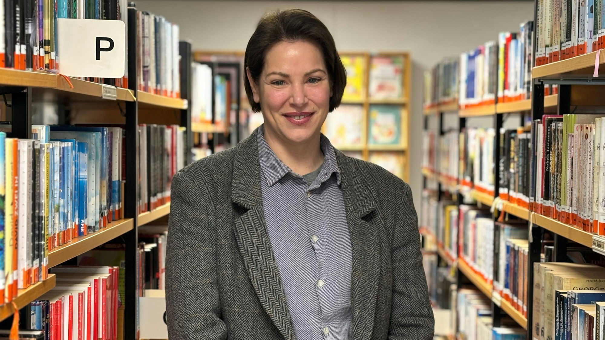 Tessa Mars steht zwischen zwei Reihen von Bücherregalen und lächelt in die Kamera.