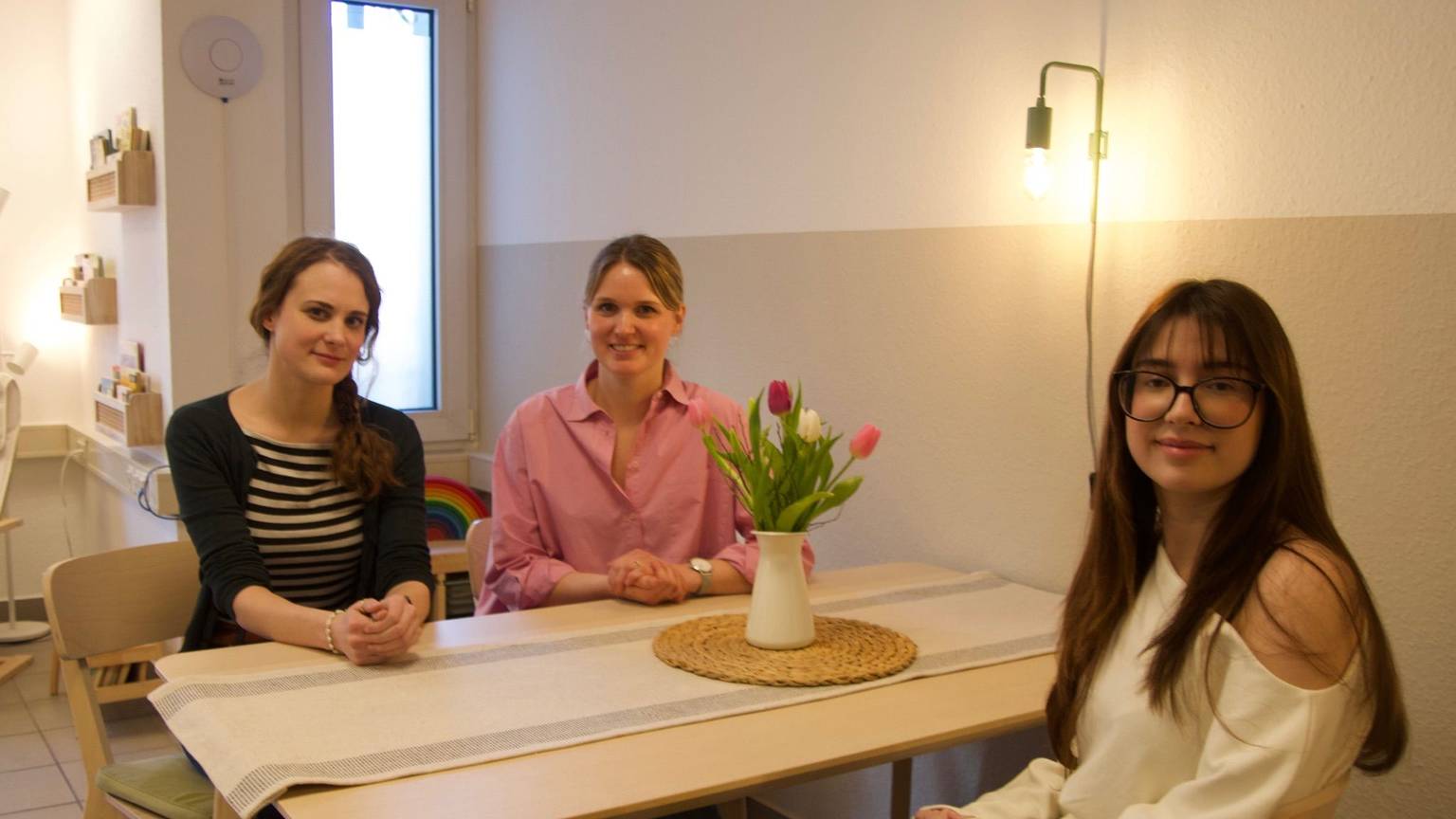 Drei Frauen sitzen an einem Tisch mit einem Strauß Blumen.