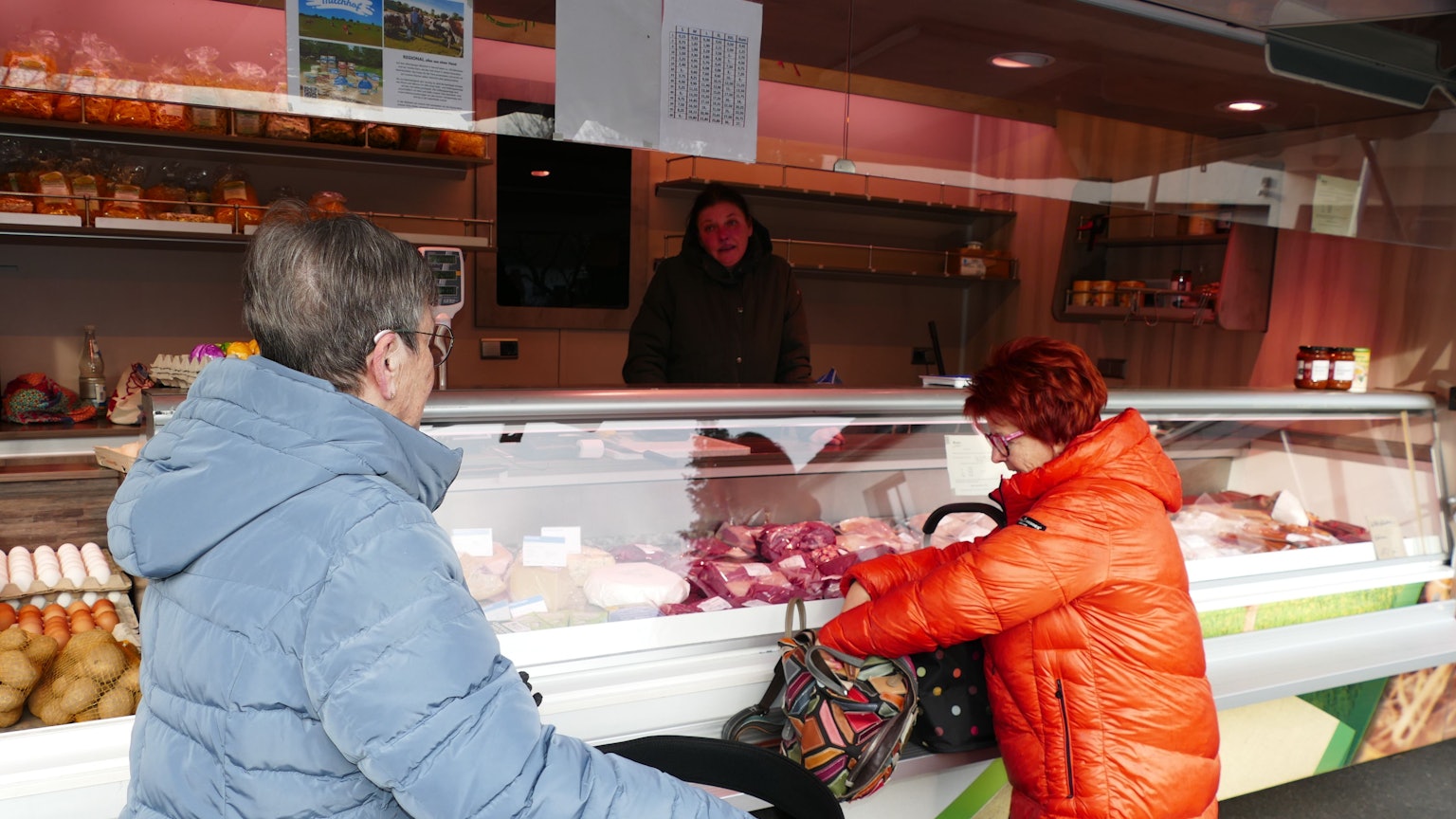 Zwei Frauen stehen vor einem Marktstand in ihren Wintermänteln.