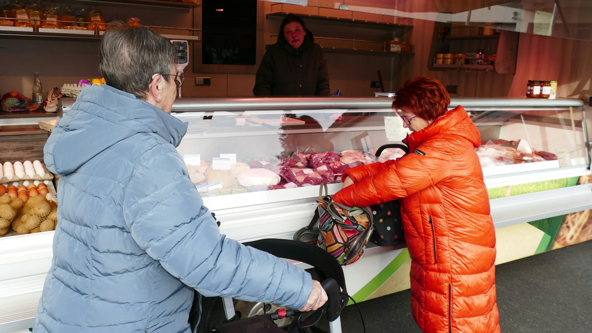 Zwei Frauen stehen vor einem Marktstand in ihren Wintermänteln.