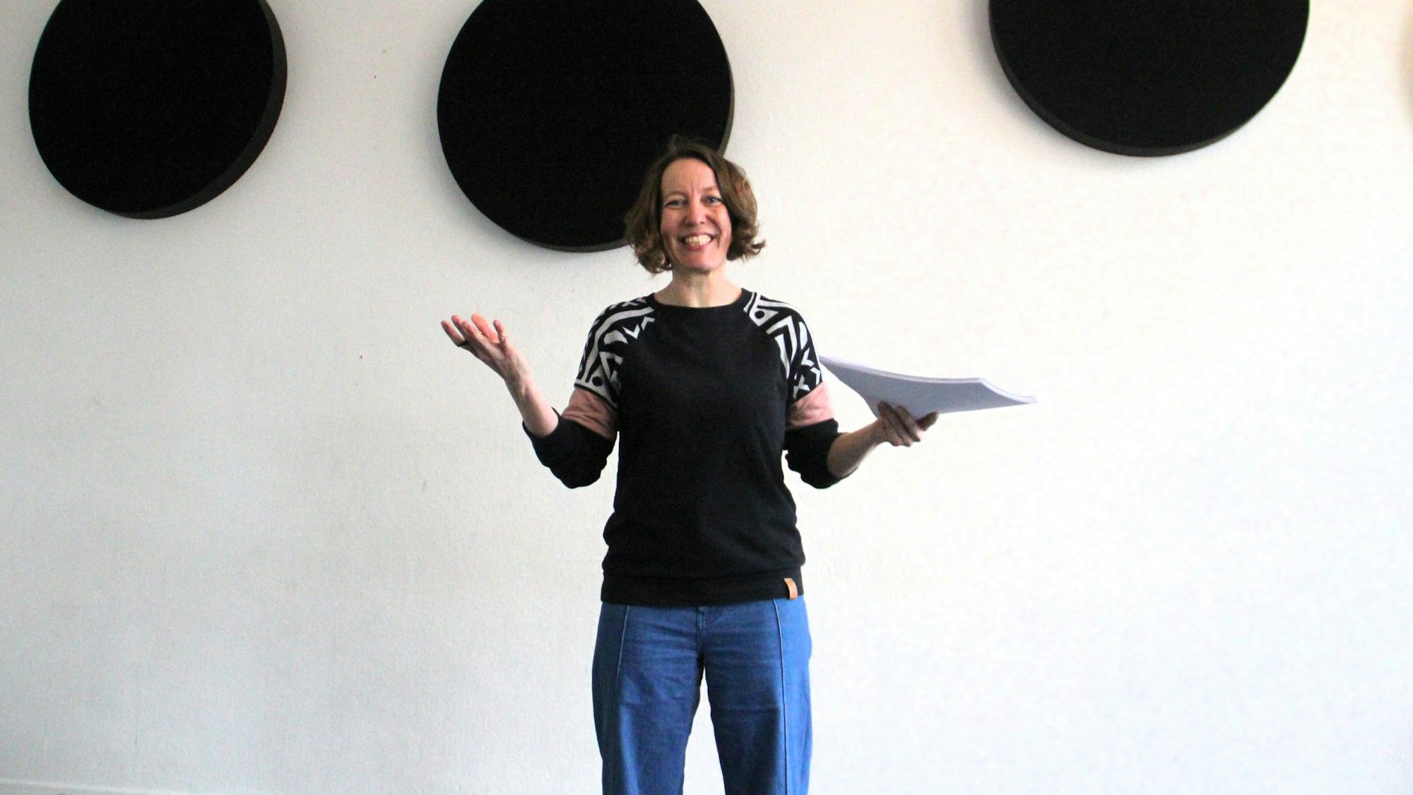 Eine Frau mit dunklem Haar steht vor einer Wand.