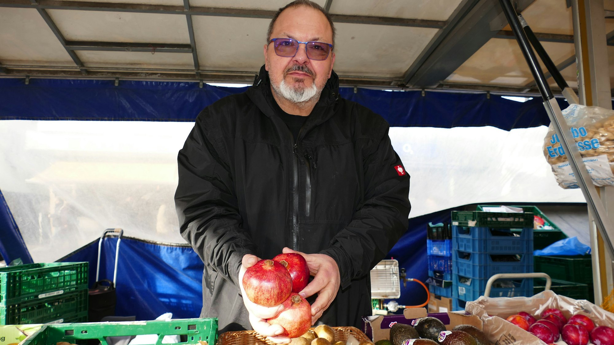 Ugur Sezer steht hinter seinem Stand und hölt drei Granatäpfel in den Händen. Er blickt in die Kamera.