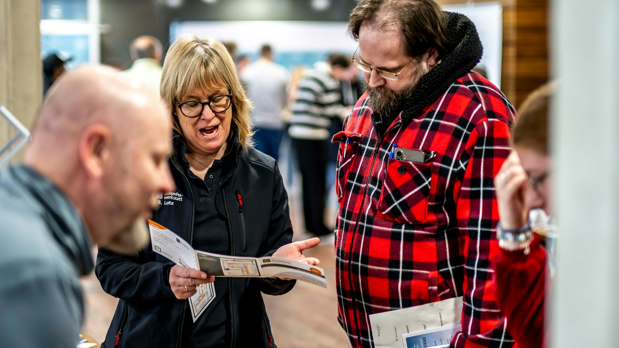 Das Bild zeigt einen Moment währen der Weiterbildungsmesse. Eine Frau erklärt einem Mann etwas in einem Info-Flyer.