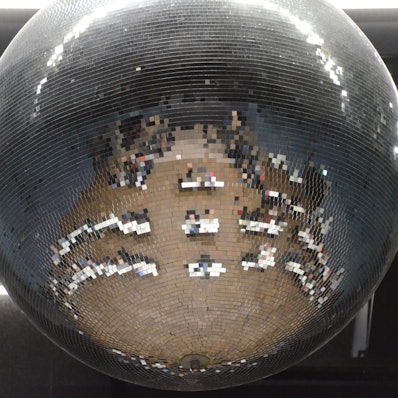 Tische und Stühle einer Gremiensitzung spiegeln sich in einer Discokugel.