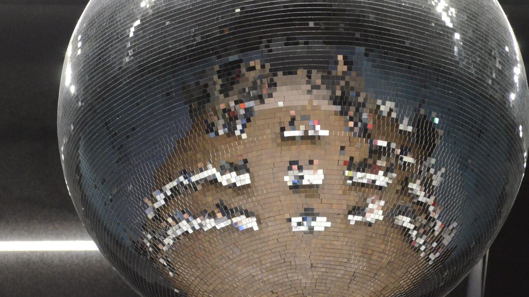 Tische und Stühle einer Gremiensitzung spiegeln sich in einer Discokugel.