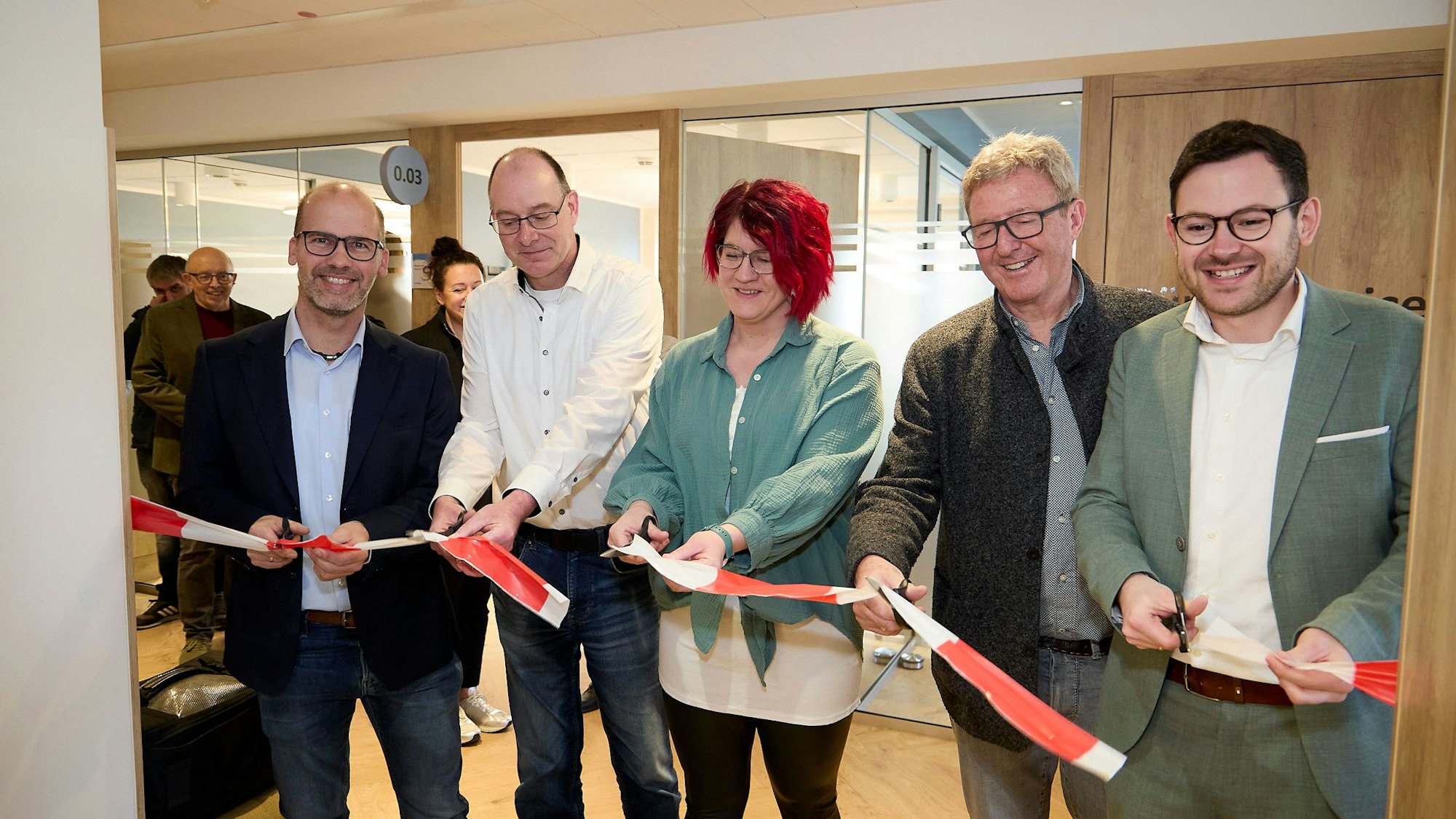 Die Genannten schneiden mit Scheren an mehreren Stellen ein rot-weißes Band durch.