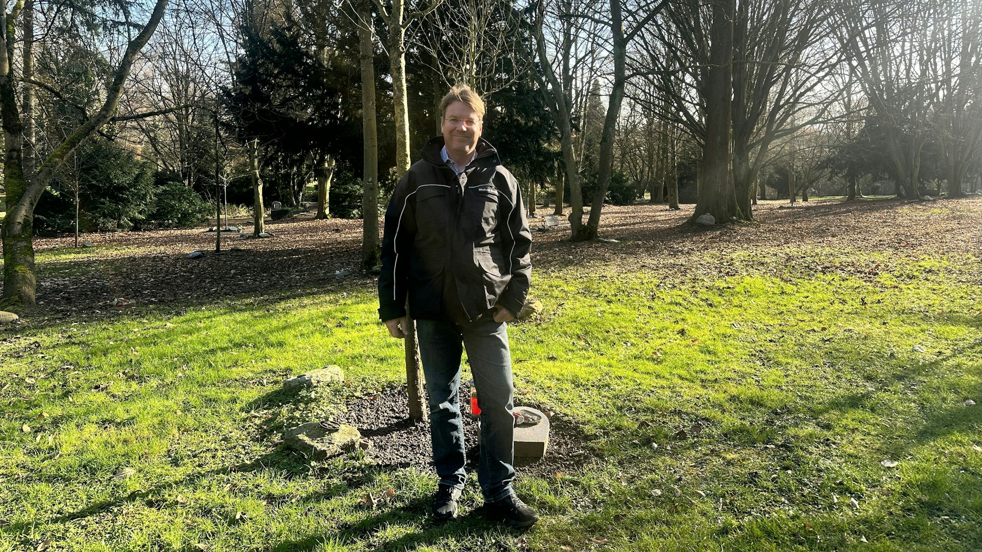 Ein Mann steht vor einer Grabstätte an einem Setzling.