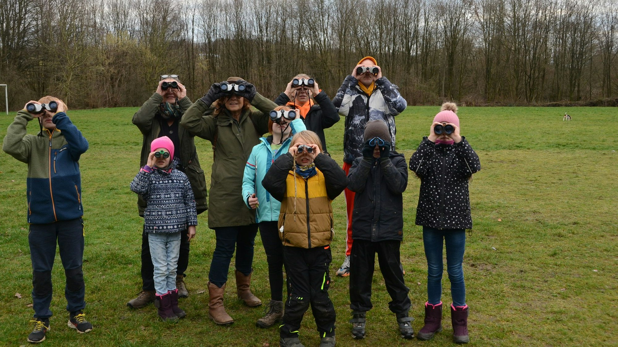 Kinder und Erwachsene stehen auf einer Wiese und blicken durch ein Fernglas.