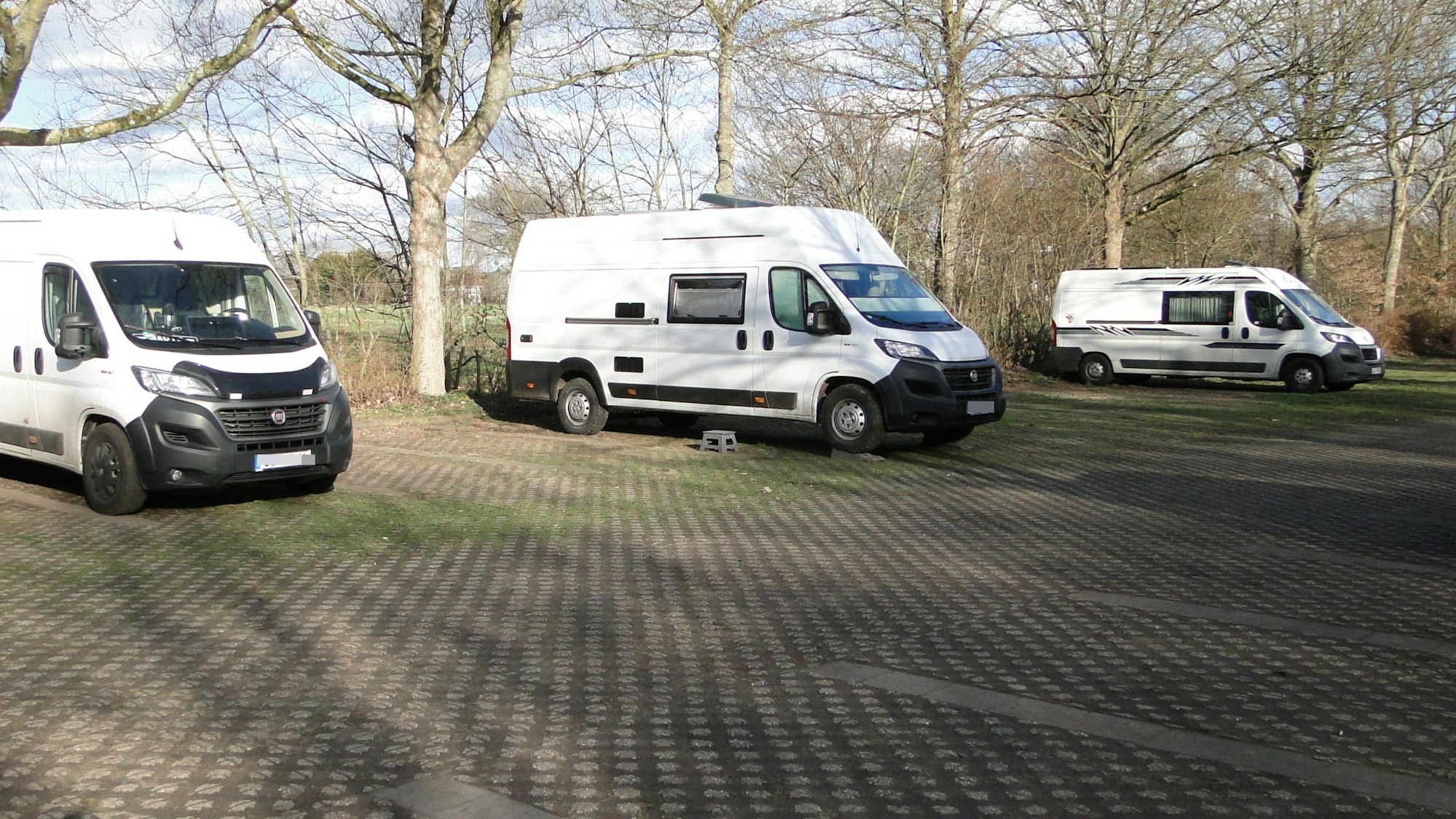 Drei Wohnmobile stehen auf einem großflächigen Parkplatz.
