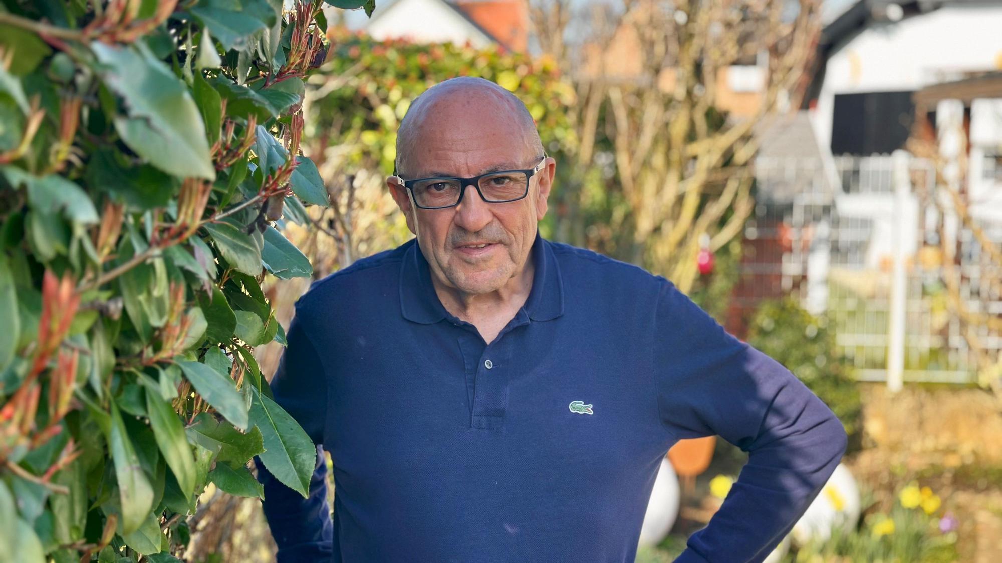 Ein Mann steht neben einer Hecke in einem Garten.