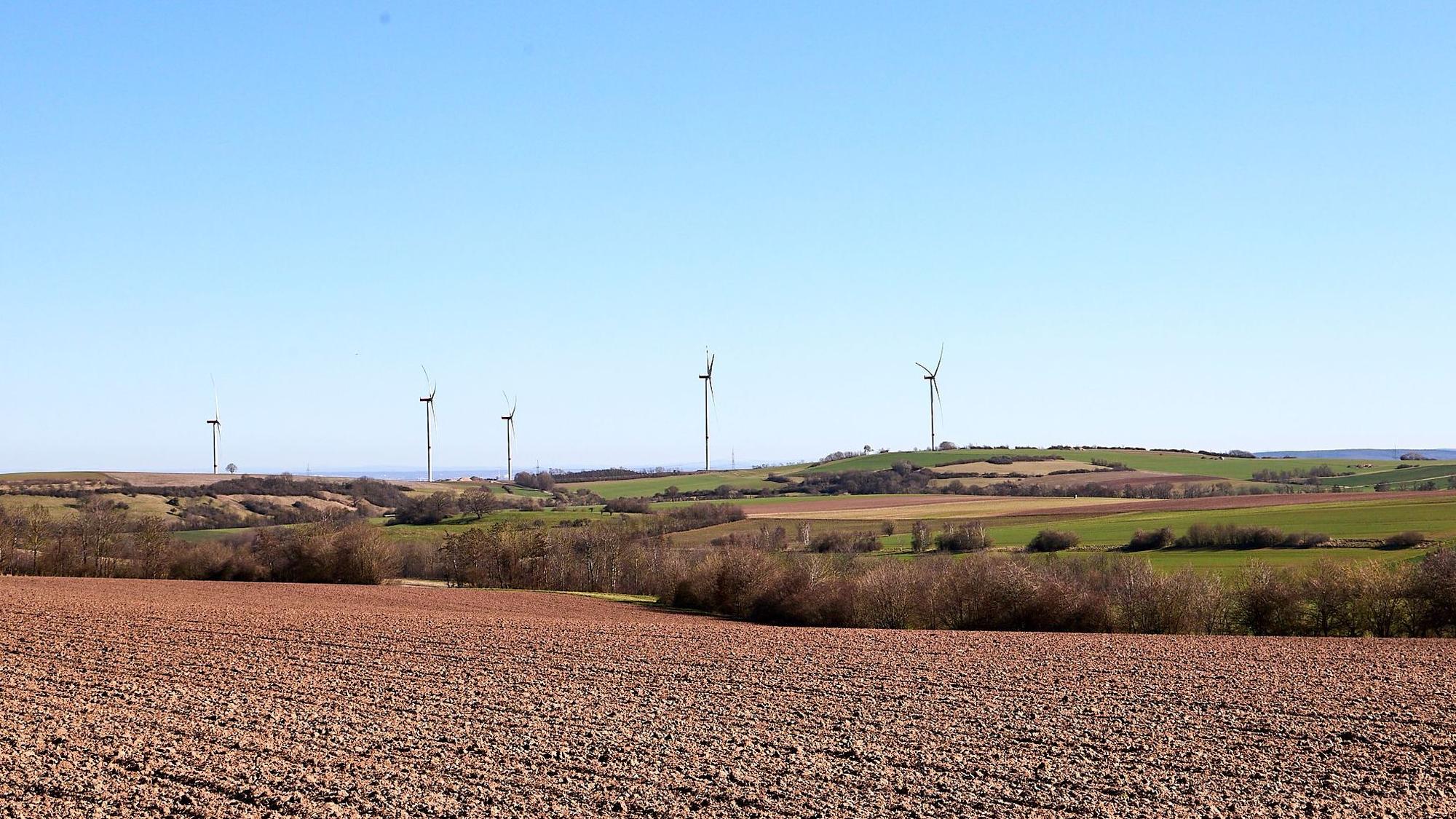 Das Bild zeigt die Eifellandschaft mit Windkraftanlagen im Hintergrund.