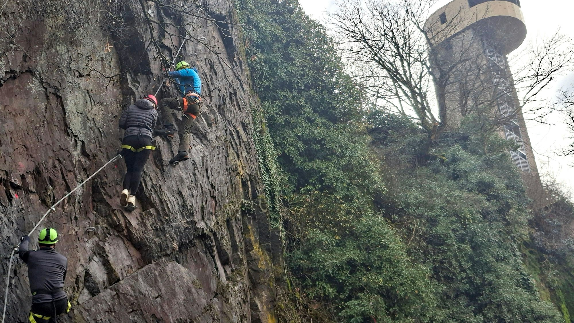 Drei Kletterer begehen in Neuerburg (Eifelkreis Bitburg-Prüm) einen Klettersteig an einer steilen Felswand.