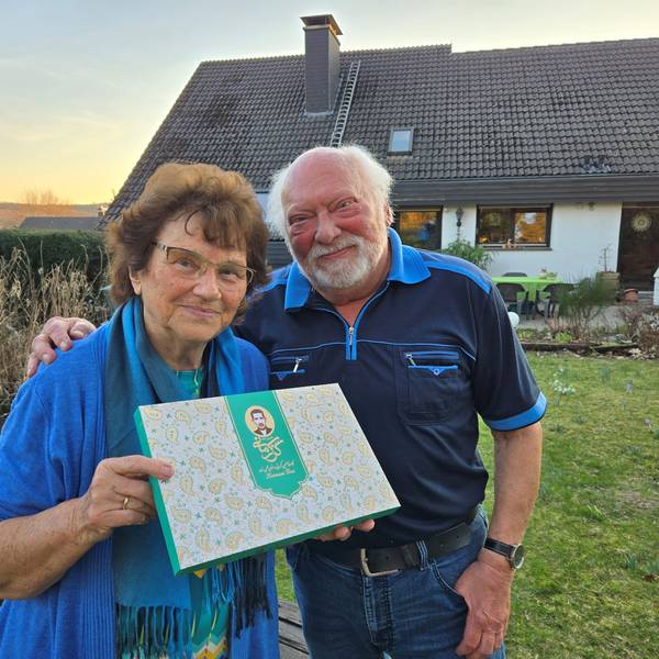 Ein älteres Ehepaar steht vor seinem Haus, sie hält eine Schachtel.