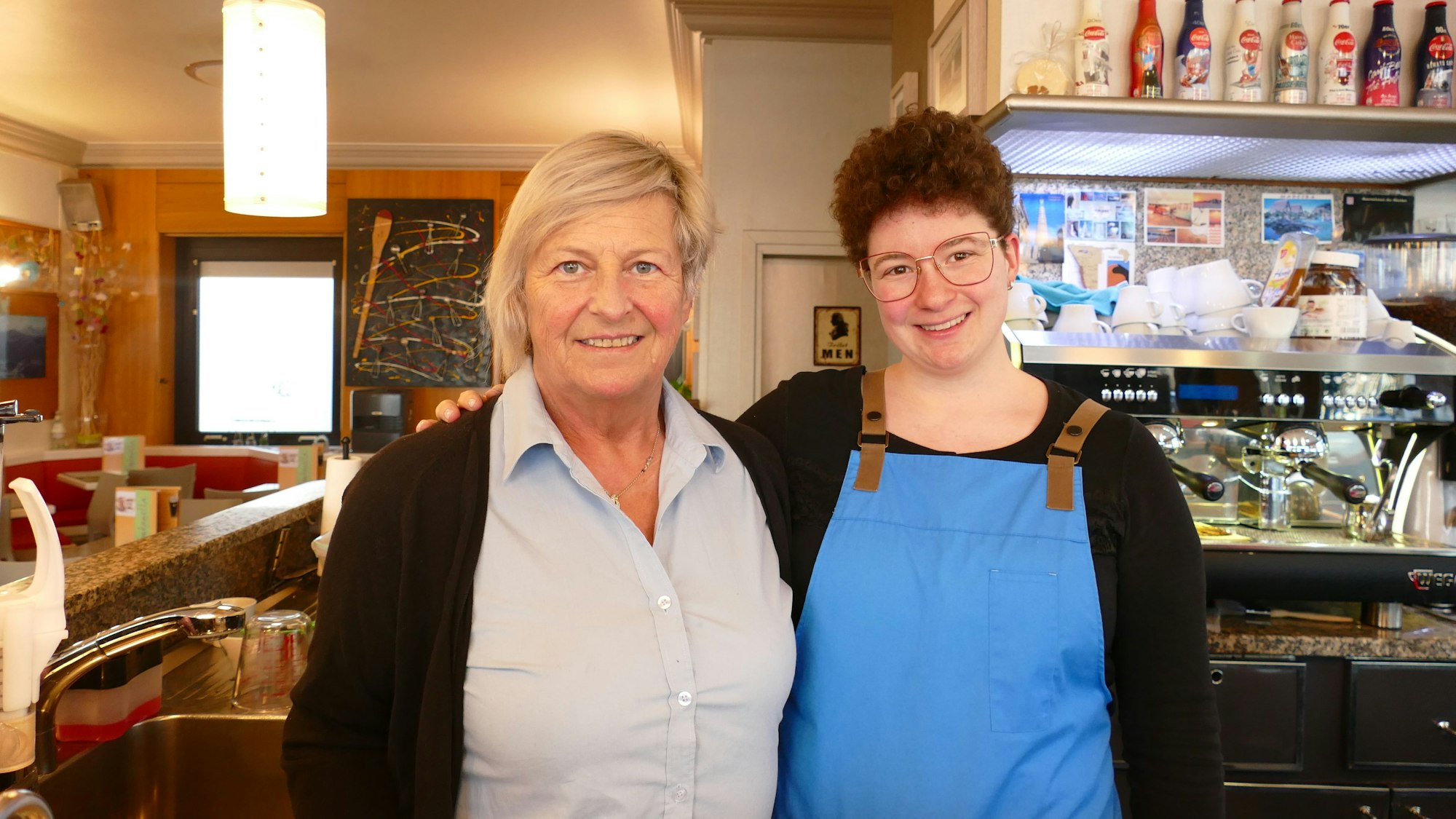 Die beiden Frauen blicken lächelnd in die Kamera. Die Nichte trägt eine blaue Schürze.