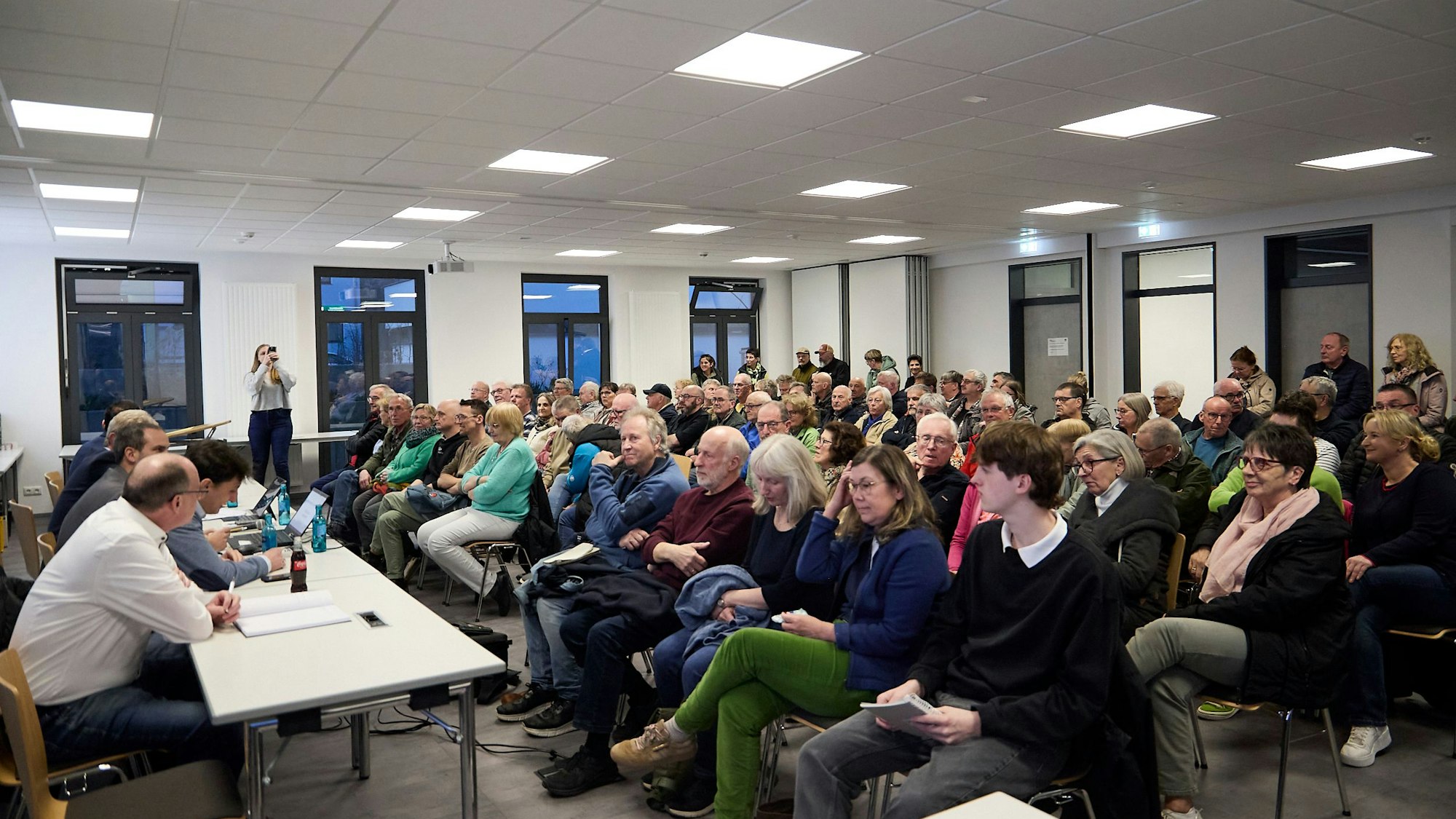 Das Foto zeigt den Versammlungsraum, in dem das Publikum in Reihen sitzt.