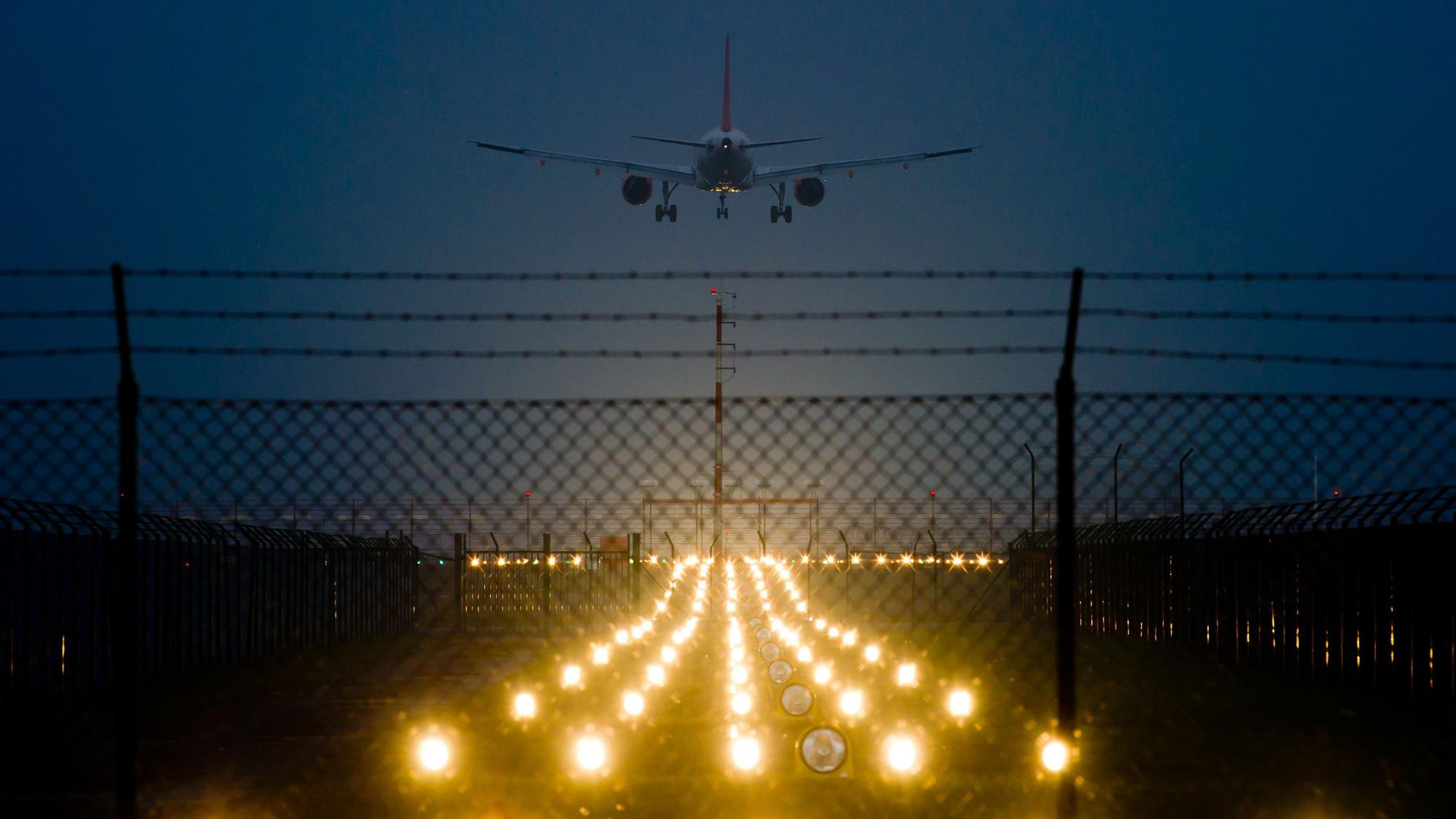 Nacht. eine beleuchtete Landebahn und ein Flugzeug im Anflug.