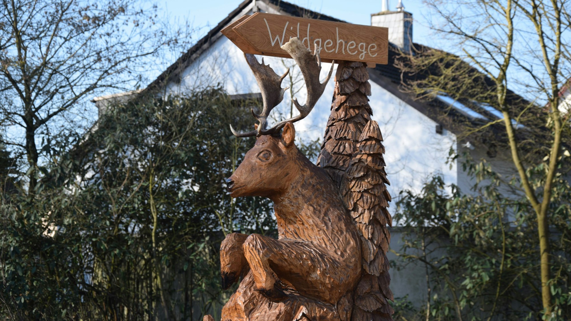 Eine Hirsch-Holzfigur trägt ein echtes Geweih auf dem Kopf.
