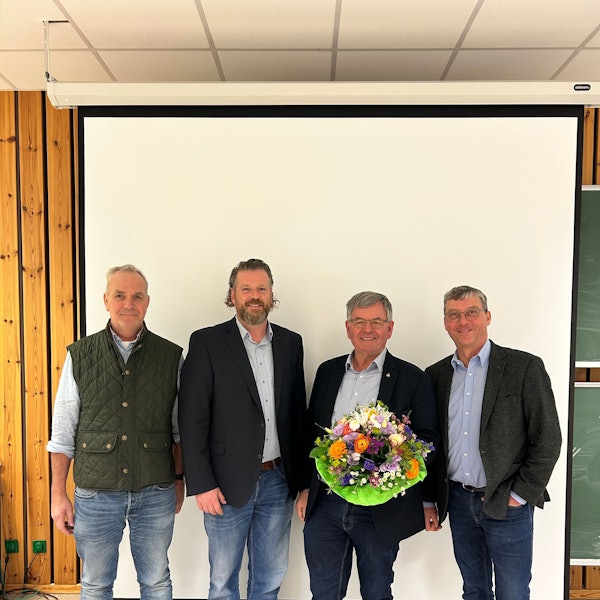 Vier Männer lächeln, einer hält einen Blumenstrauß.